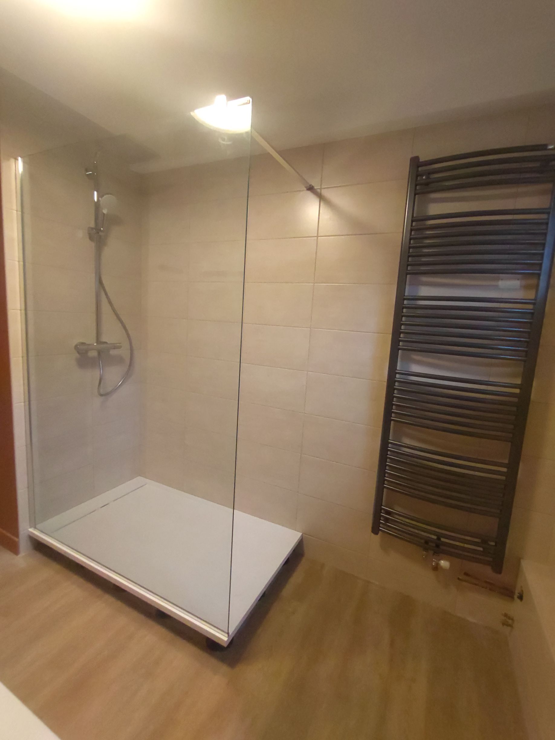 Salle de bains avec cabine de douche, sèche-serviettes chauffant et murs carrelés de couleur claire.