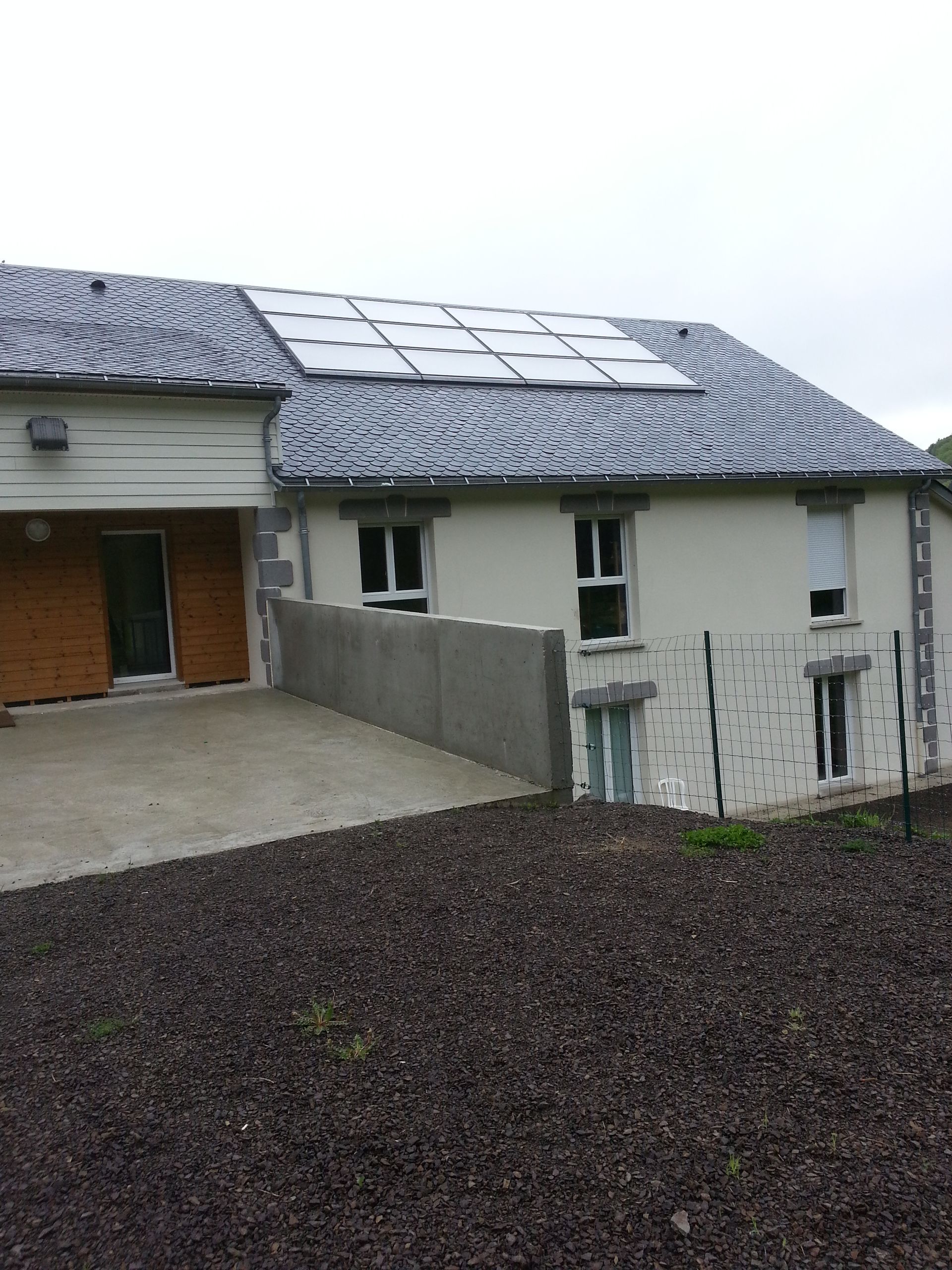 Bâtiment avec panneaux solaires sur un toit gris, murs blancs et rampe en béton.