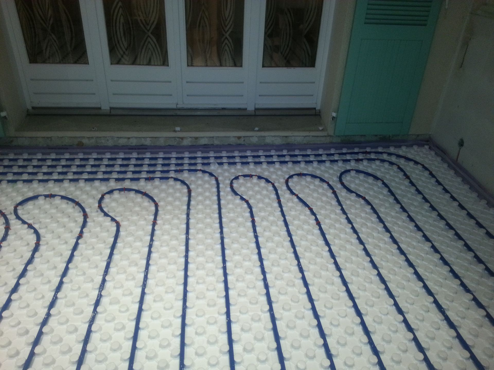 Des tubes bleus posés sur un isolant blanc, prêts pour un système de chauffage au sol radiant.