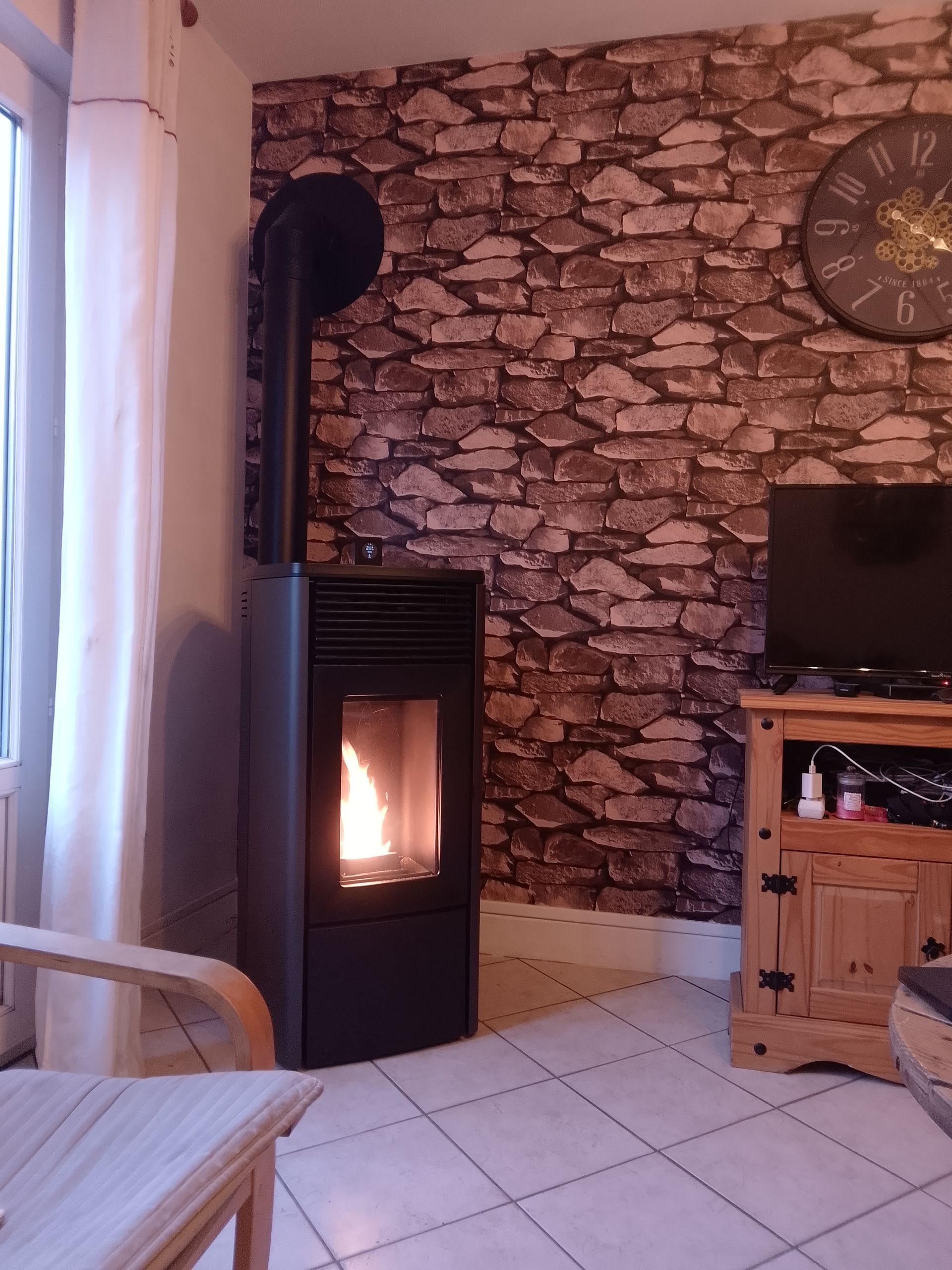 Poêle à granulés noirs avec des flammes contre un mur en pierre dans un salon.