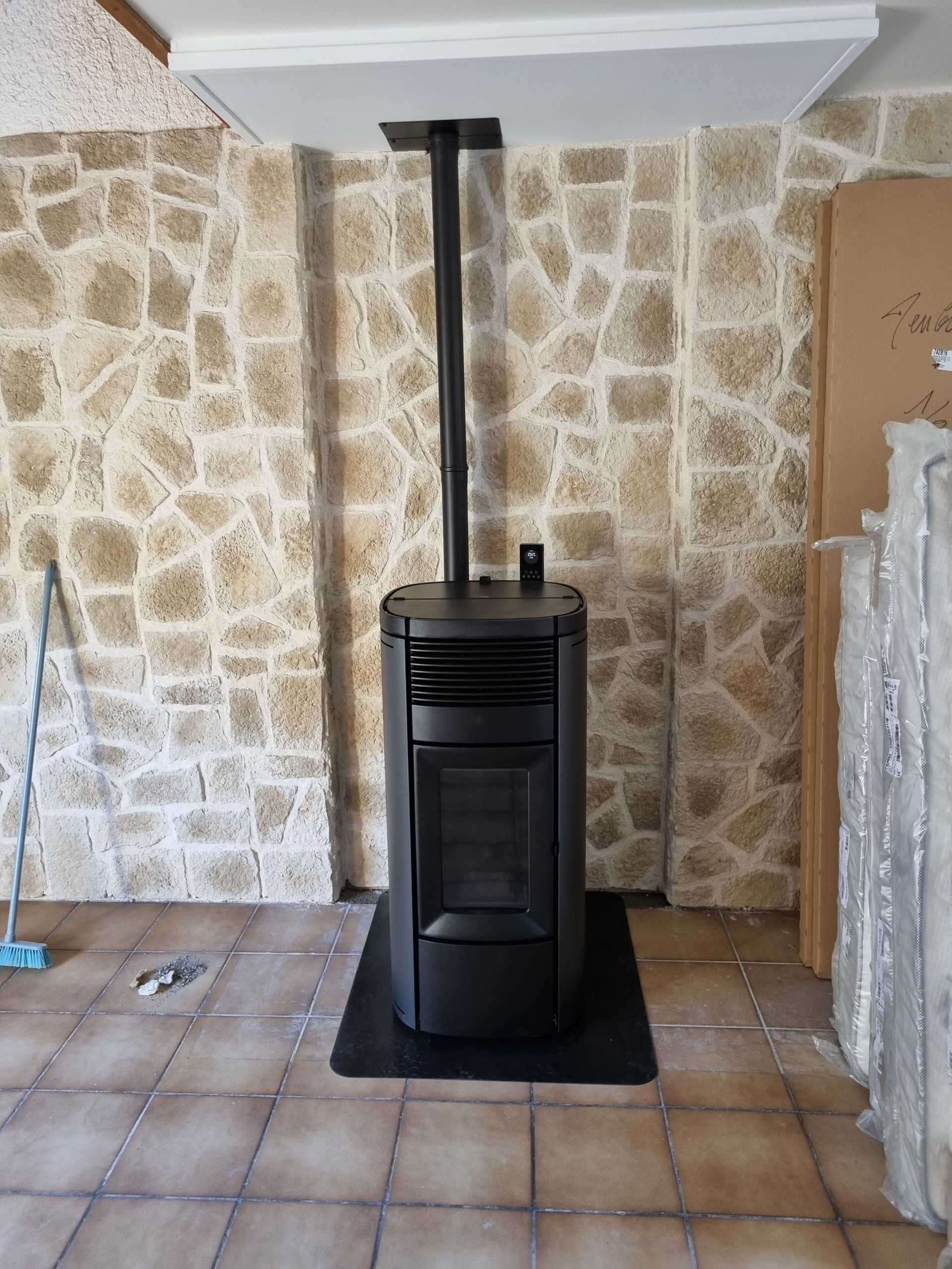 Poêle à granulés noirs avec conduit vertical contre un mur en pierre dans une pièce.