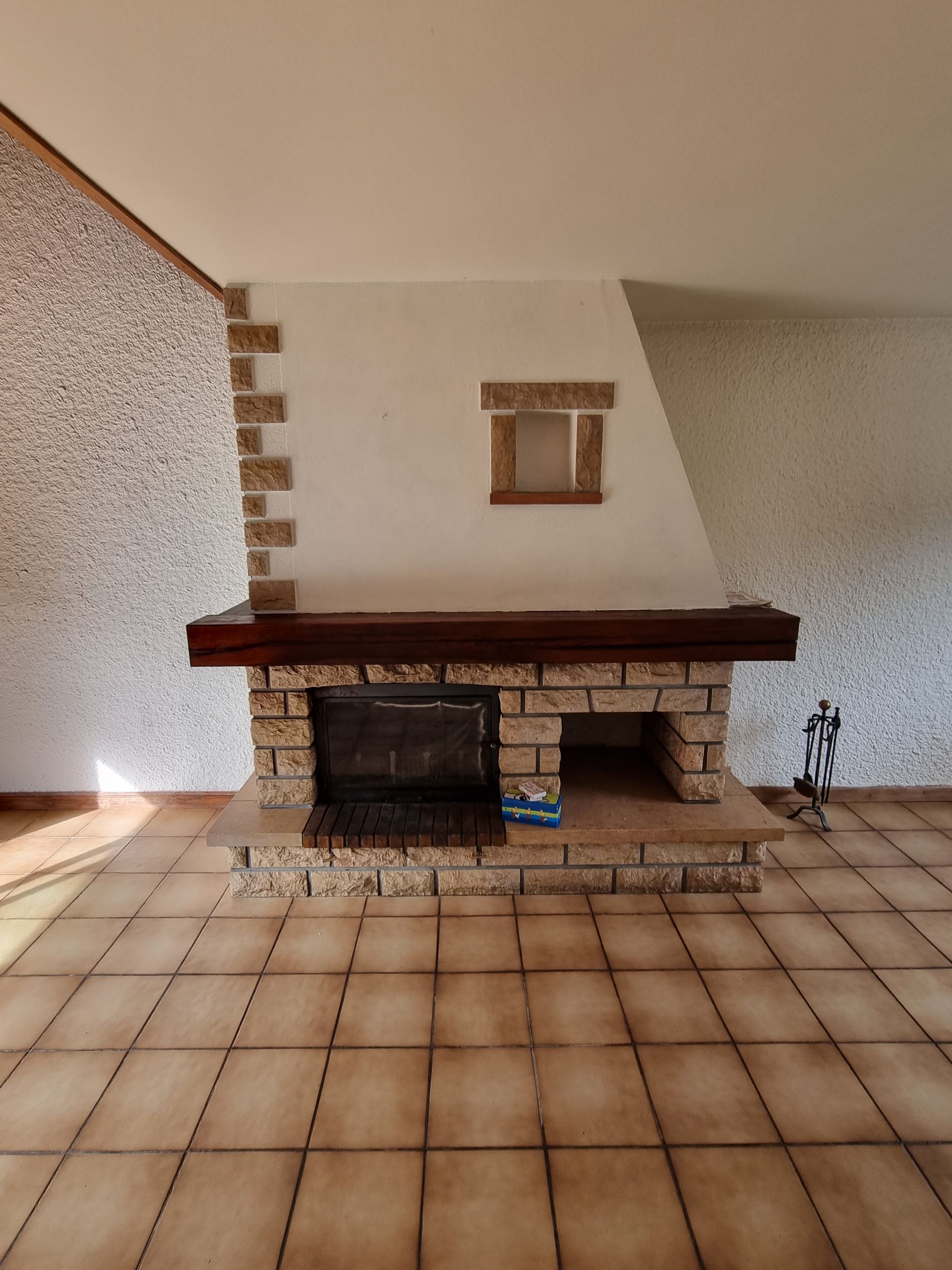 Cheminée en pierre brun clair, manteau en bois foncé et petite fenêtre décorative au-dessus de l'ouverture du foyer.