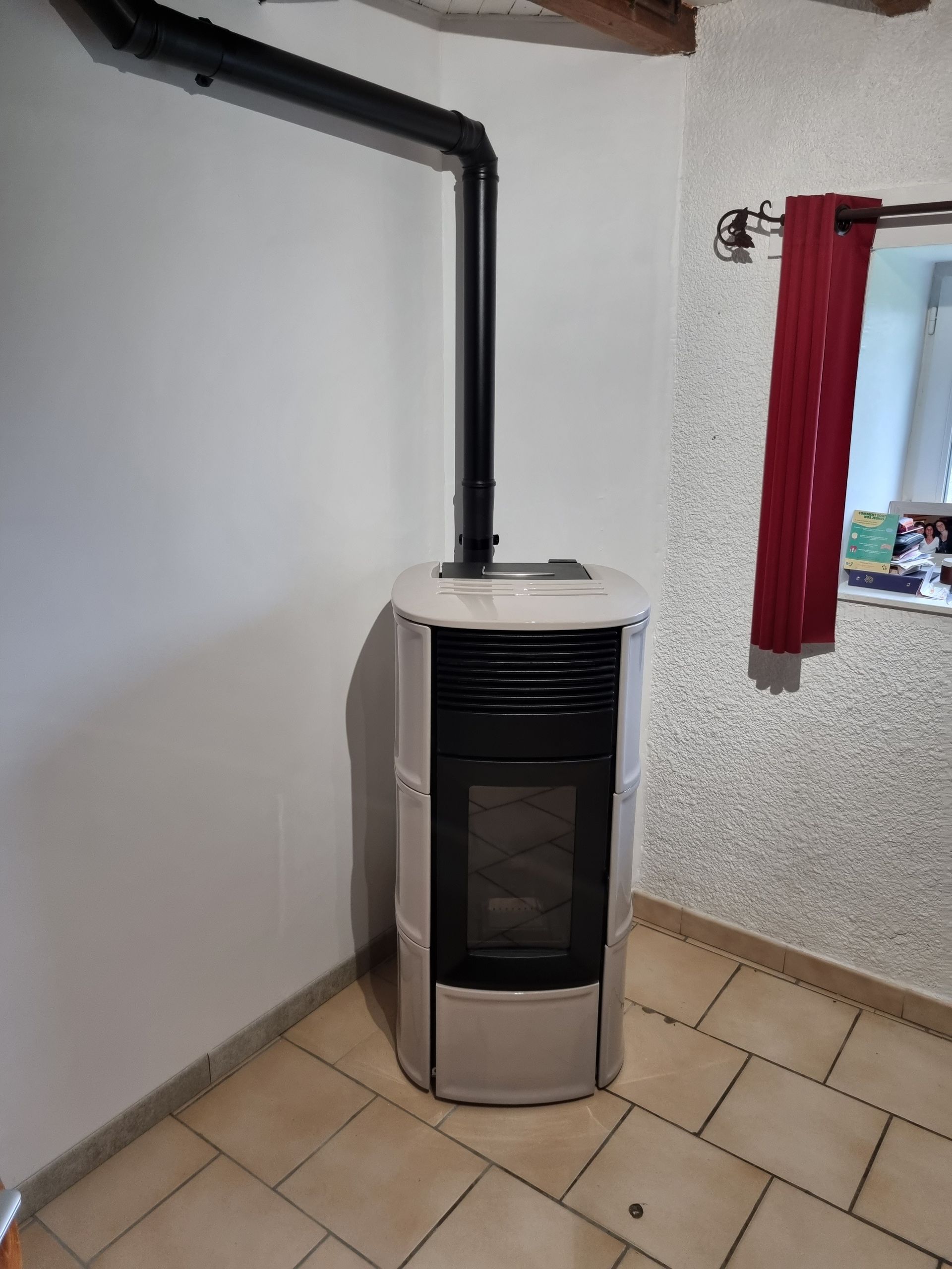 Un poêle à granulés avec un conduit de cheminée noir, installé dans un coin avec un rideau rouge.