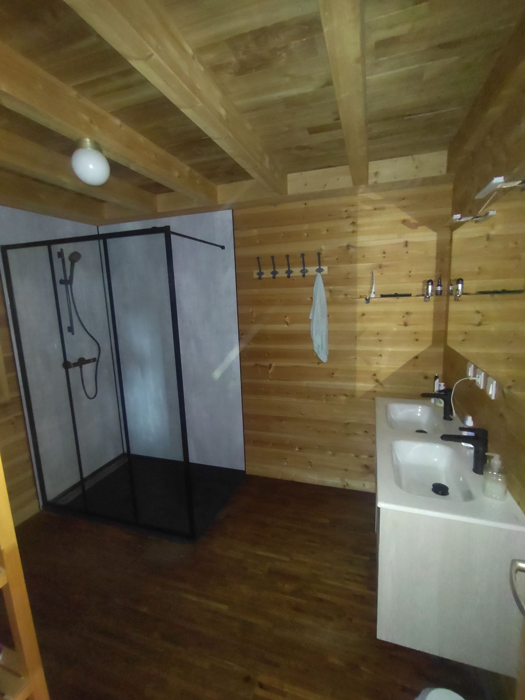 Salle de bains avec murs et plafond en bois, douche en verre et meuble-lavabo blanc.