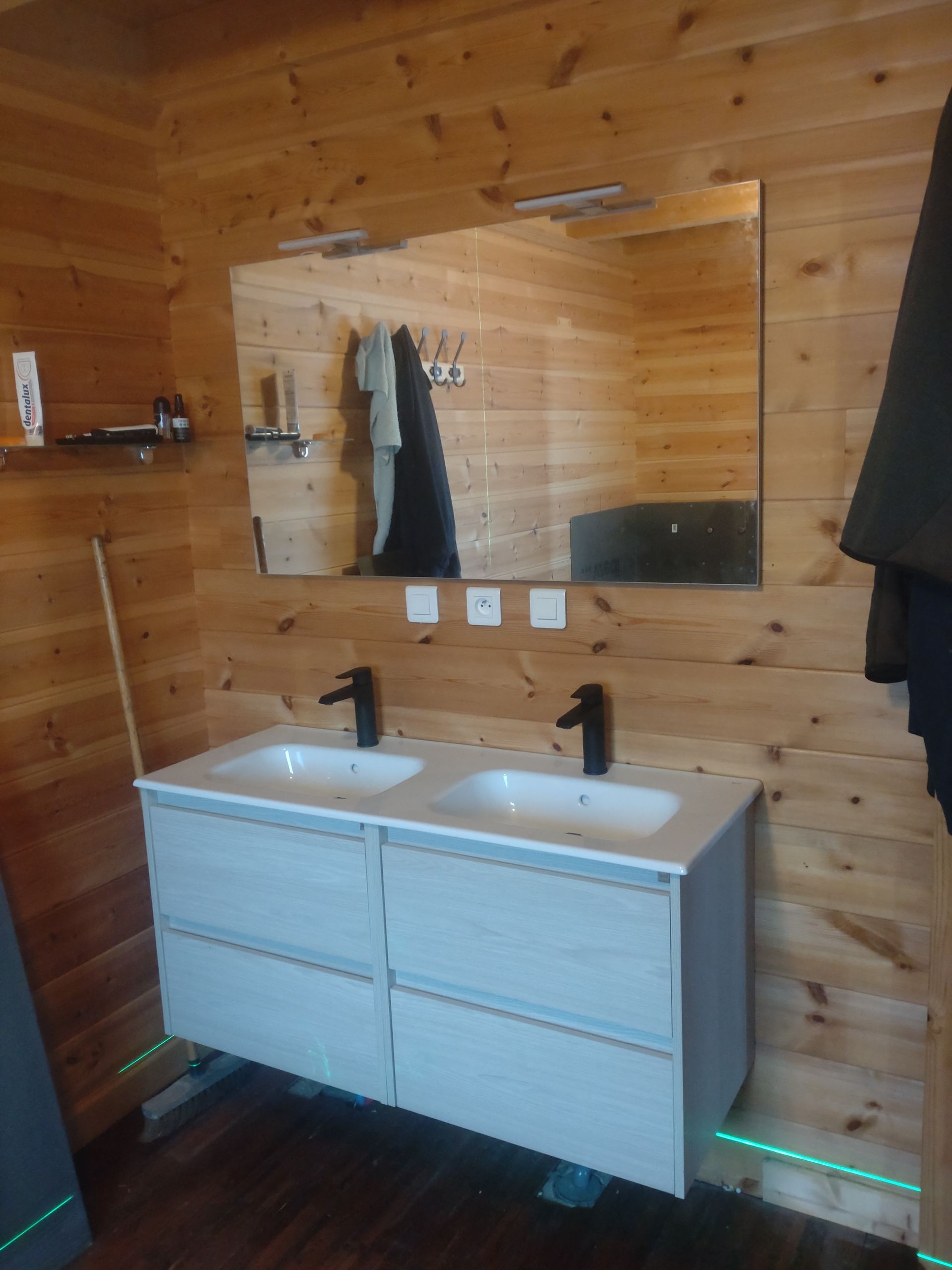 Salle de bains avec lambris, double vasque avec robinetterie noire et grand miroir.