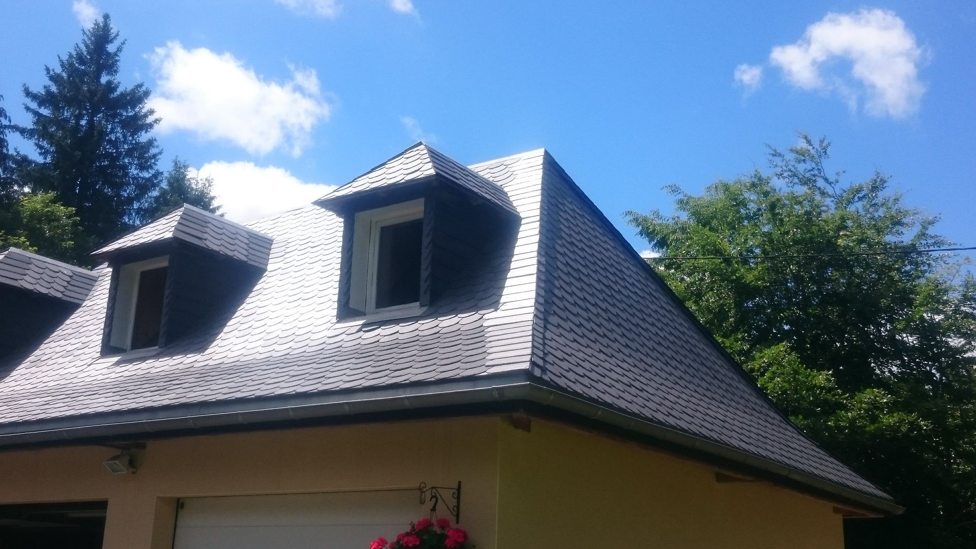 Une maison avec un toit en bardeaux gris foncé, des lucarnes et un ciel bleu en arrière-plan.
