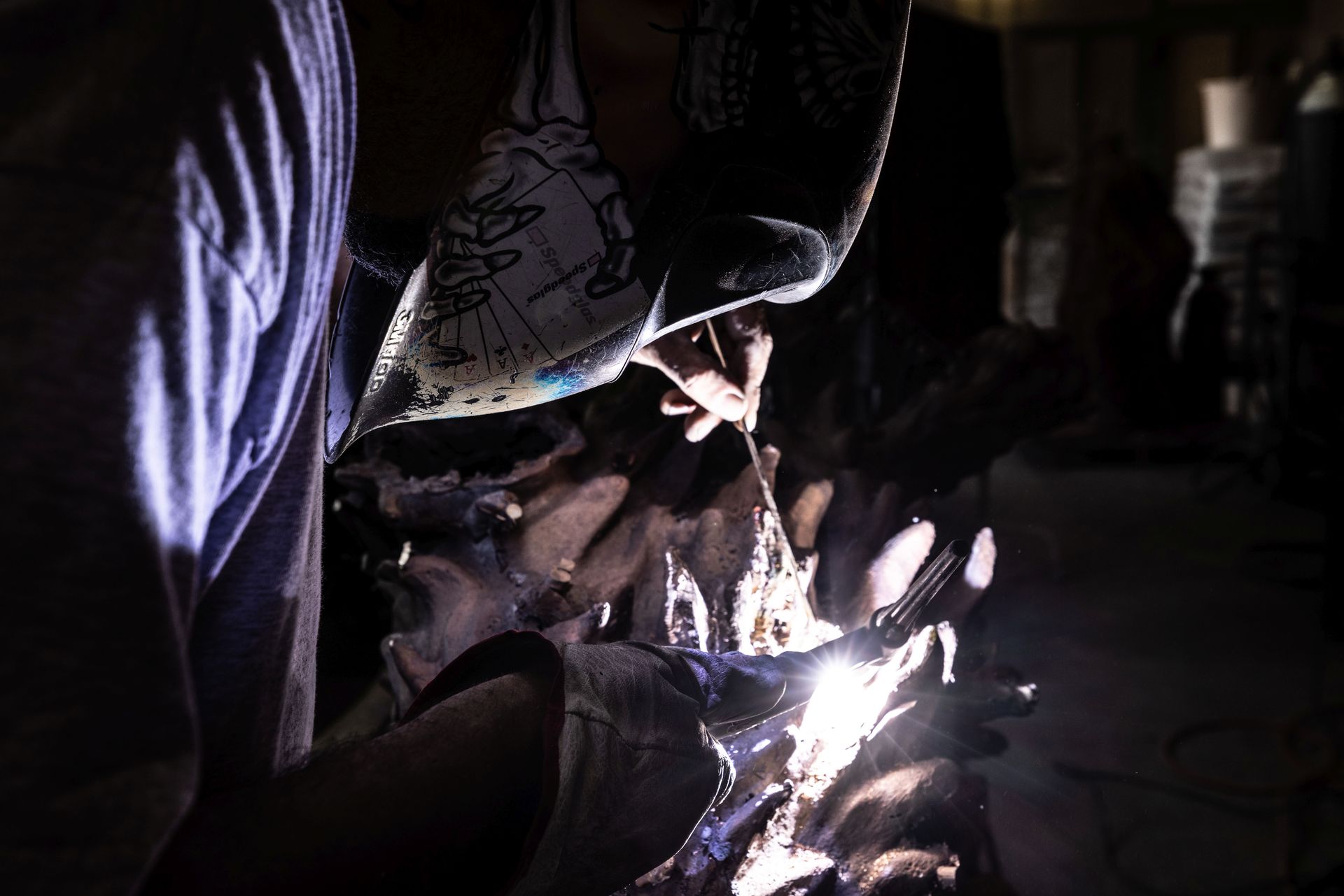 Un uomo sta saldando un pezzo di metallo in una stanza buia.