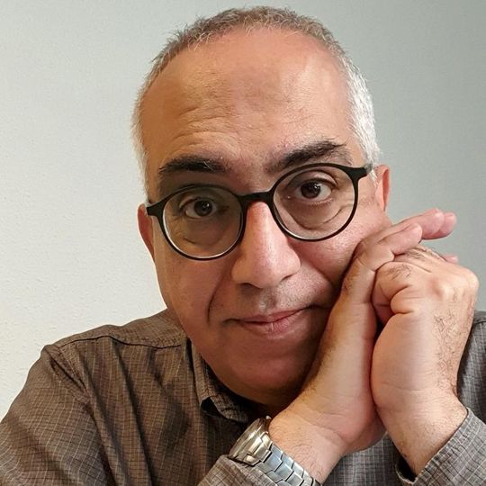 Primer plano de una persona con gafas, que apoya la cara en las manos con expresión pensativa.