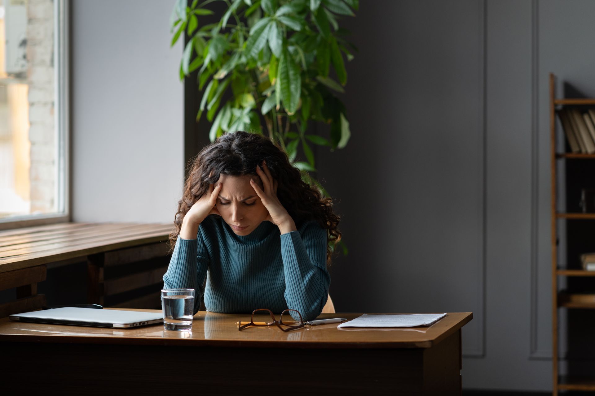 Une femme est assise à un bureau avec la tête dans ses mains.