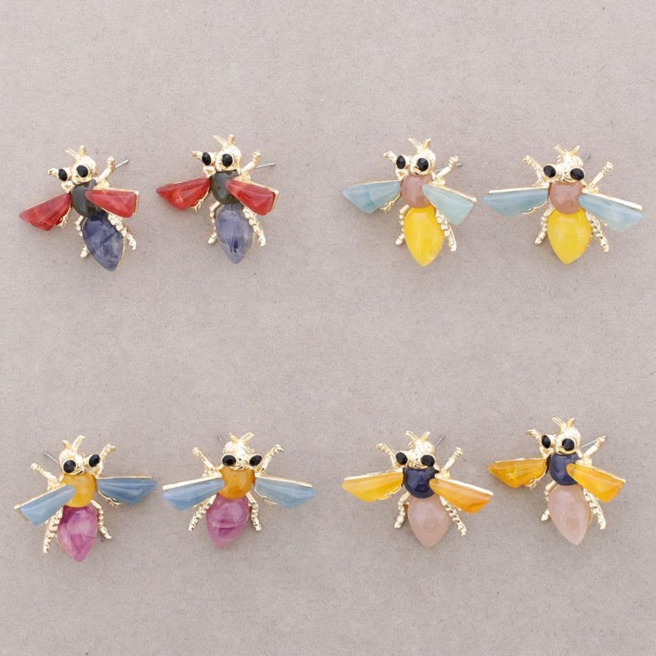 Seis pequeños broches de abeja enjoyados en rojo, azul, amarillo y rosa dispuestos sobre un fondo claro.