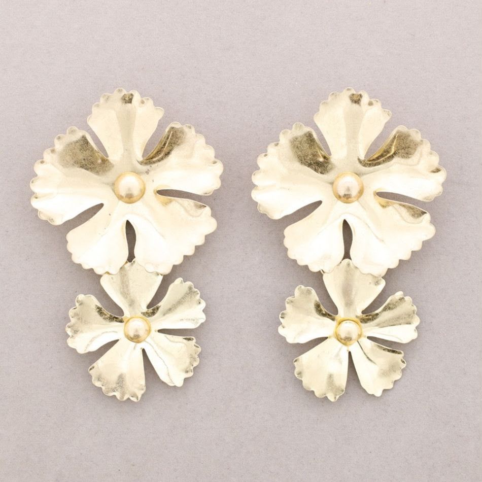 Cuatro pendientes color crema con forma de flor y centros dorados, dispuestos en forma de cuadrado sobre un fondo gris.