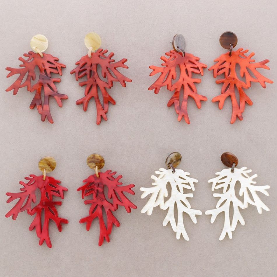 Pendientes surtidos en forma de hoja, rojos y blancos, con remaches redondos dispuestos en filas sobre un fondo claro.