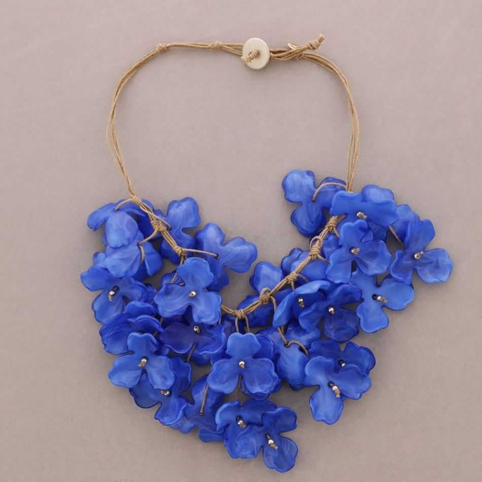 Collar con una flor azul y un racimo en forma de corazón en un cordón color canela.