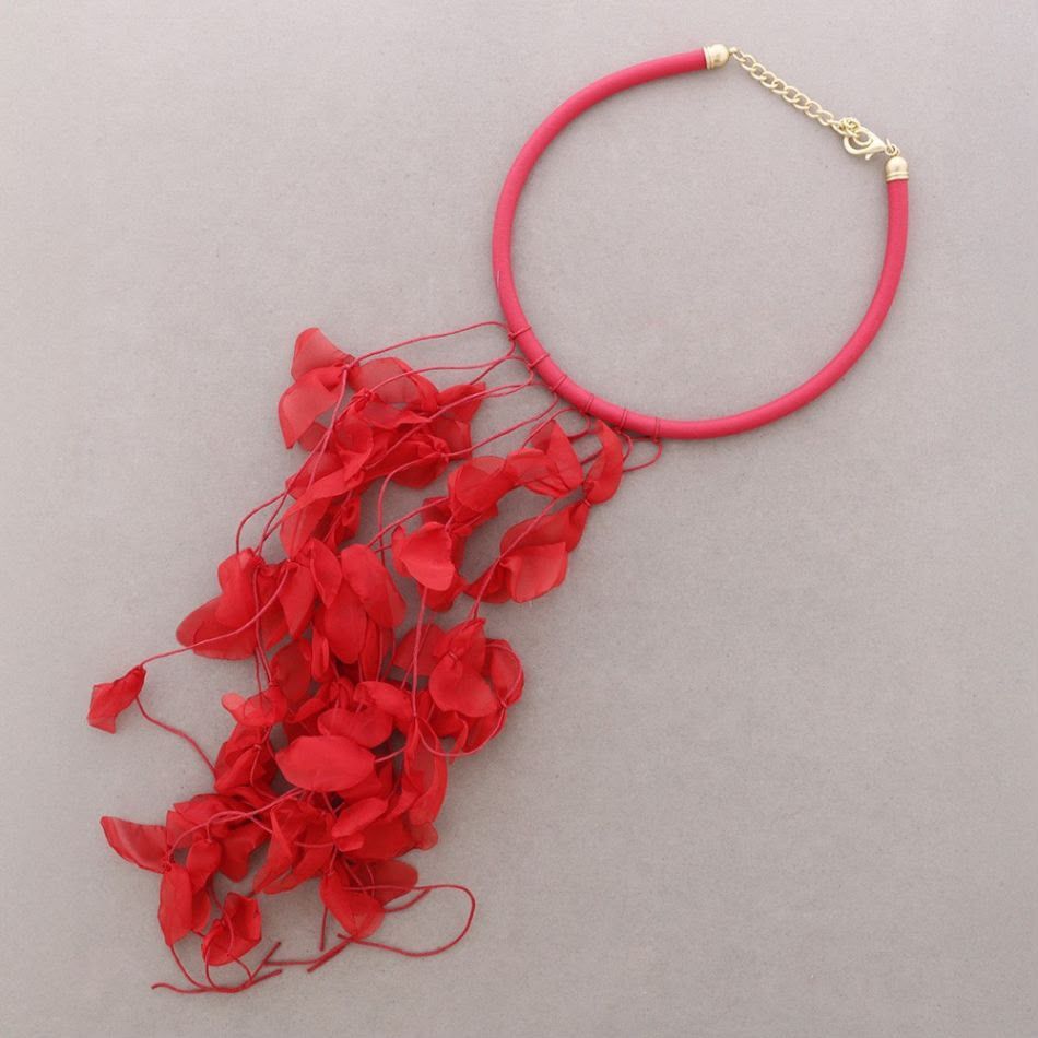 Gargantilla roja con flecos colgantes en forma de hoja roja sobre un fondo gris.