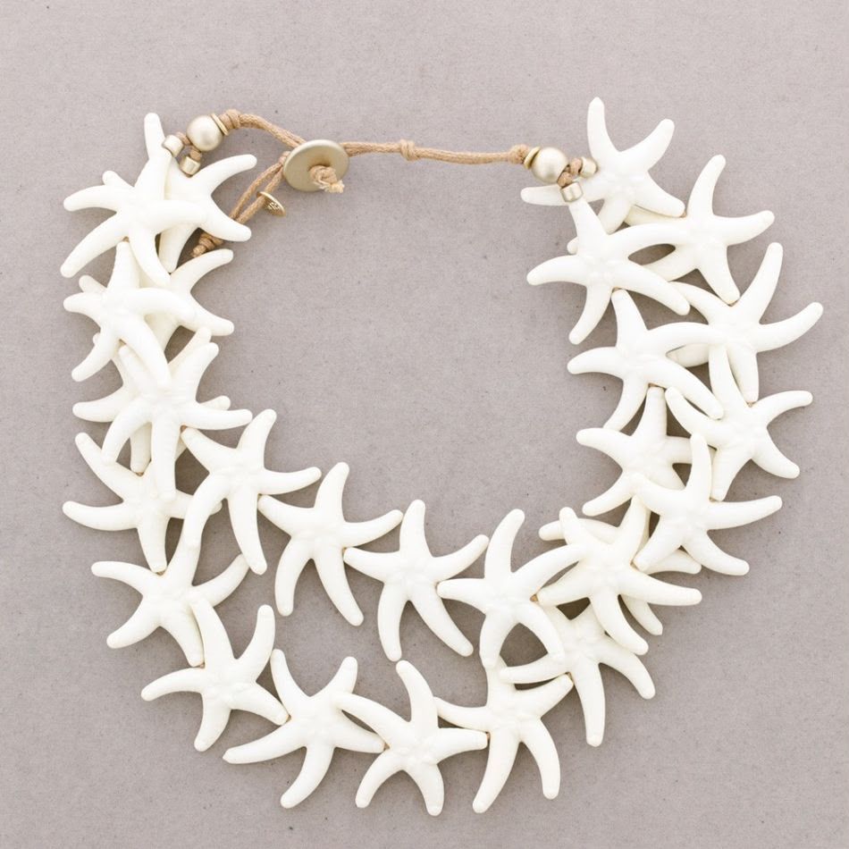 Collar con forma de estrella de mar blanca y cierre dorado sobre fondo gris claro.