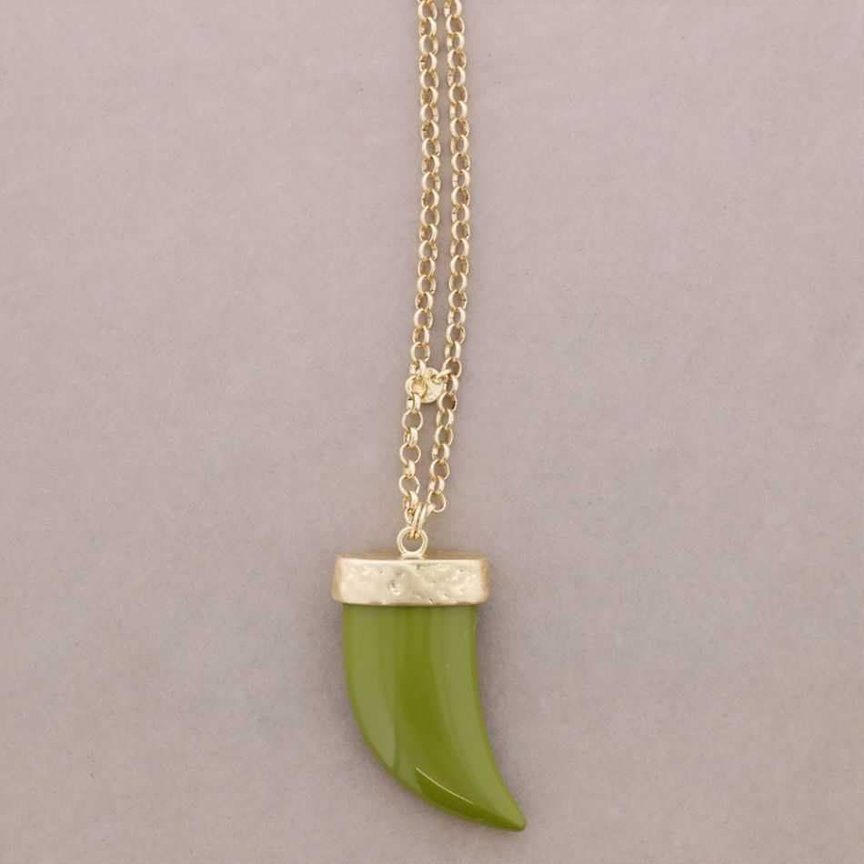Colgante verde en forma de garra sobre una cadena dorada con fondo beige.