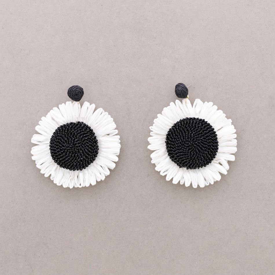Dos pendientes de margaritas en blanco y negro sobre un fondo beige.