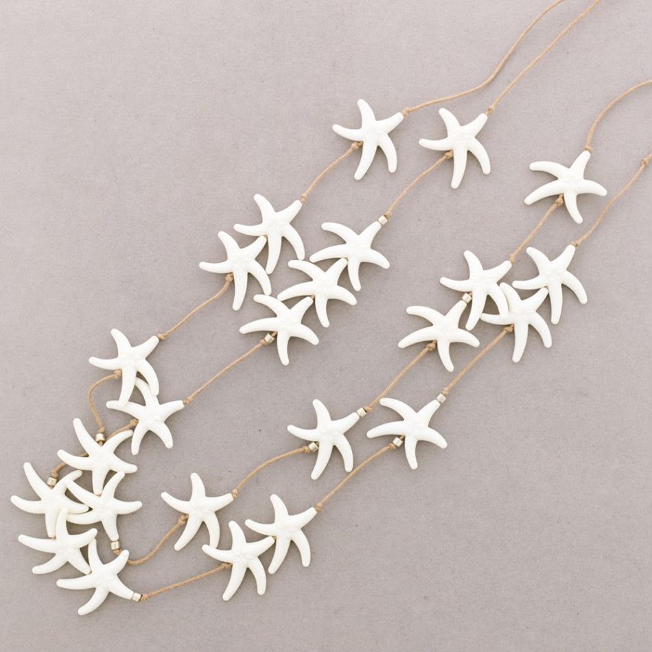Collares blancos con forma de estrella de mar en finas cadenas de oro dispuestos sobre un fondo beige claro.