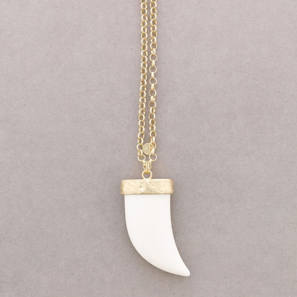 Colgante blanco con forma de colmillo en una cadena de oro sobre un fondo gris.