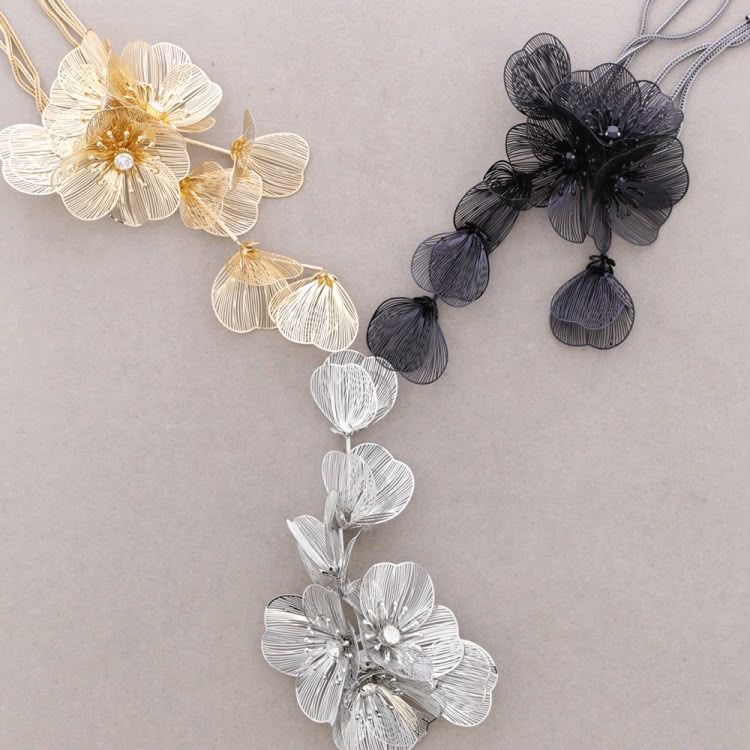 Tres collares florales con cuentas en blanco, dorado y negro sobre un fondo beige.