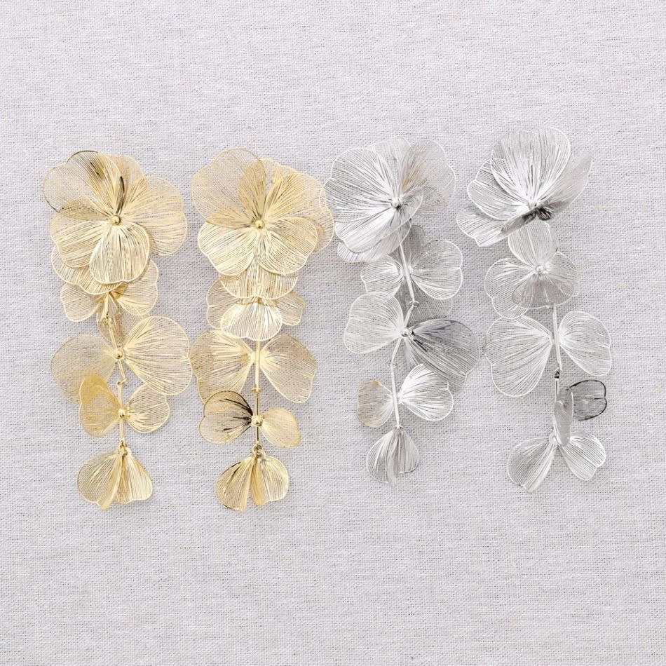 Cuatro ramitas de tallos de flores secas en amarillo pálido y plata sobre un fondo de tela clara.