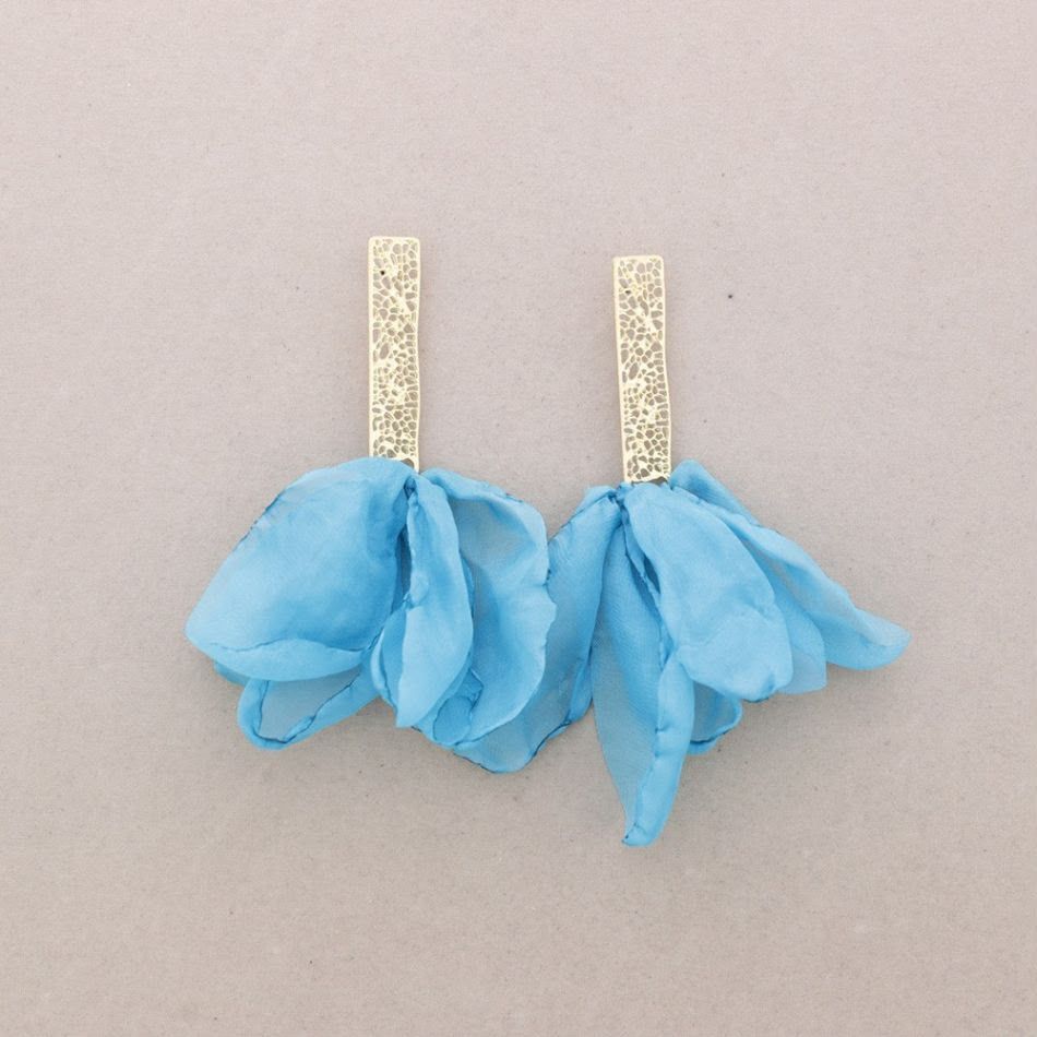 Par de pendientes azules en forma de flor con postes dorados brillantes sobre un fondo claro.