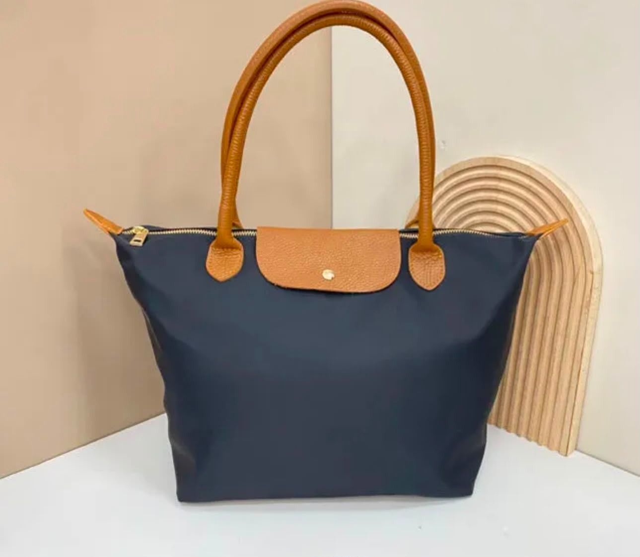 Bolso tote azul marino con asas y solapa color camel, sobre un fondo claro.