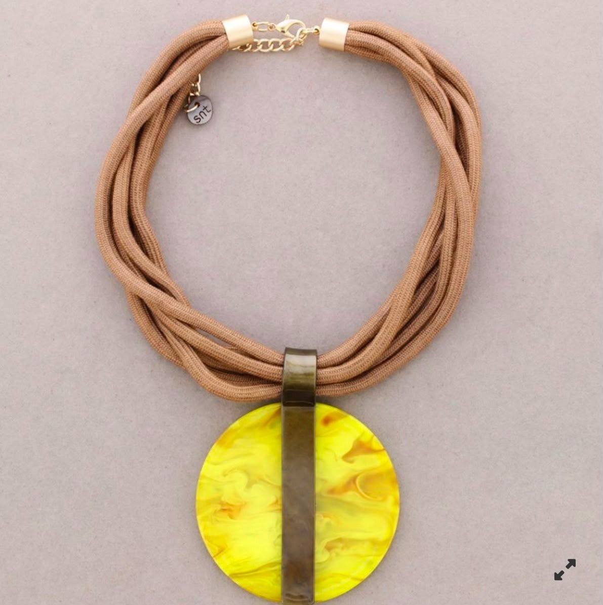 Collar de cordón color canela con un gran colgante redondo amarillo y un detalle vertical oscuro, sobre un fondo claro.