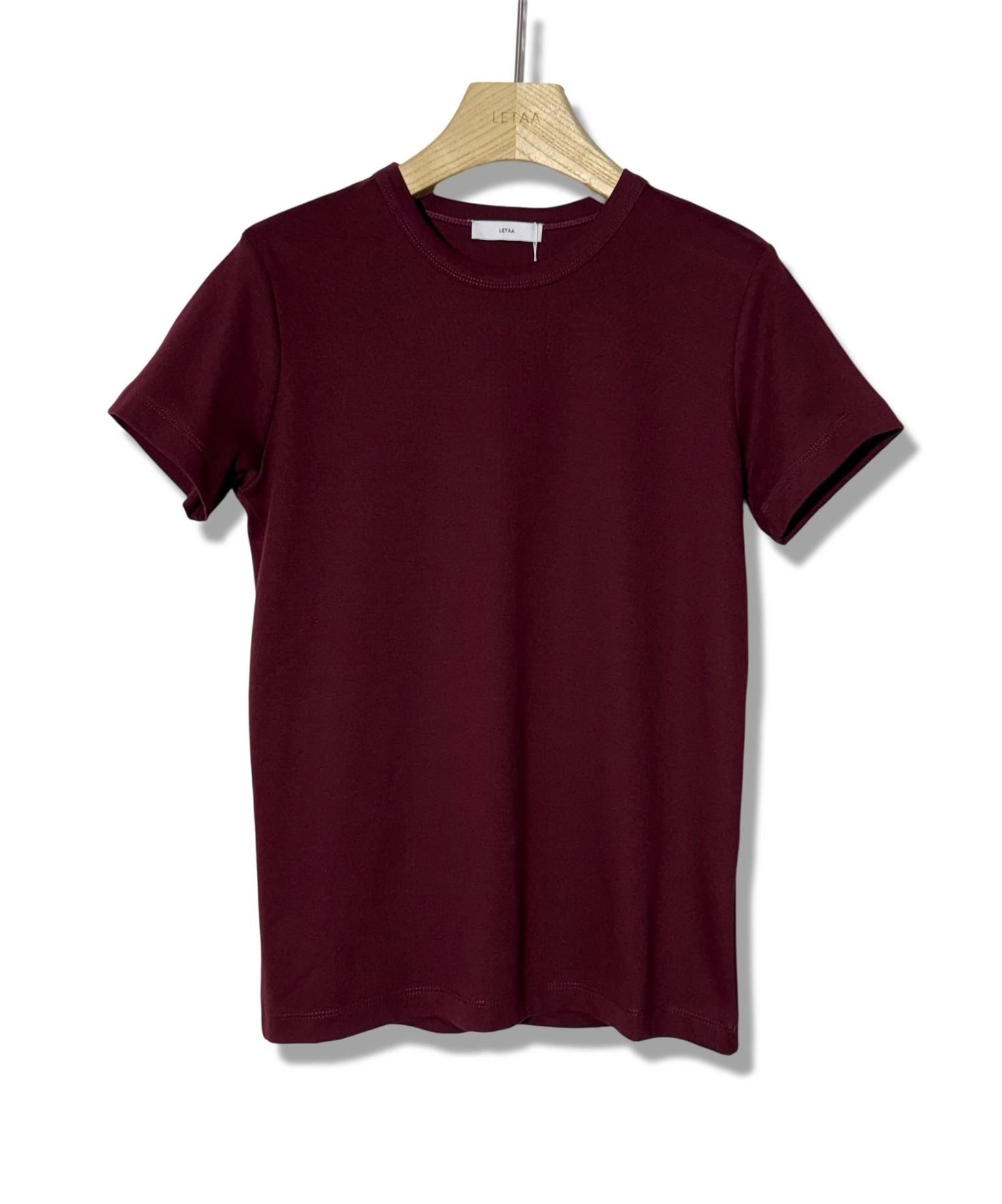 Camiseta granate colgada en una percha de madera sobre un fondo blanco.
