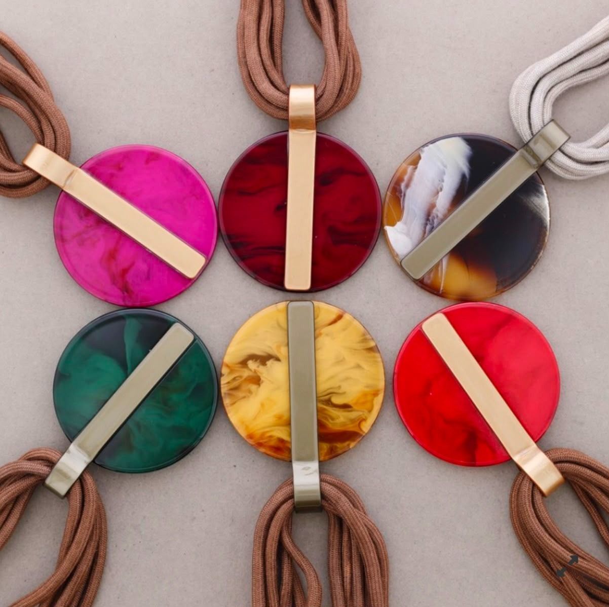 Seis coloridos collares redondos con colgantes y cordones, dispuestos en cuadrícula sobre un fondo gris.
