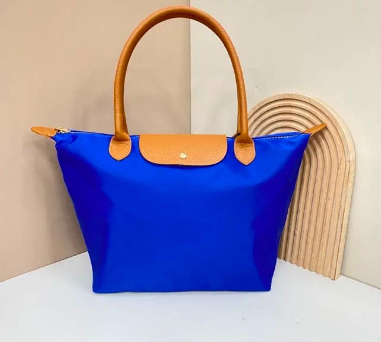 Bolso de mano azul con asas color canela sobre una superficie blanca, junto a una pieza decorativa de madera curvada.