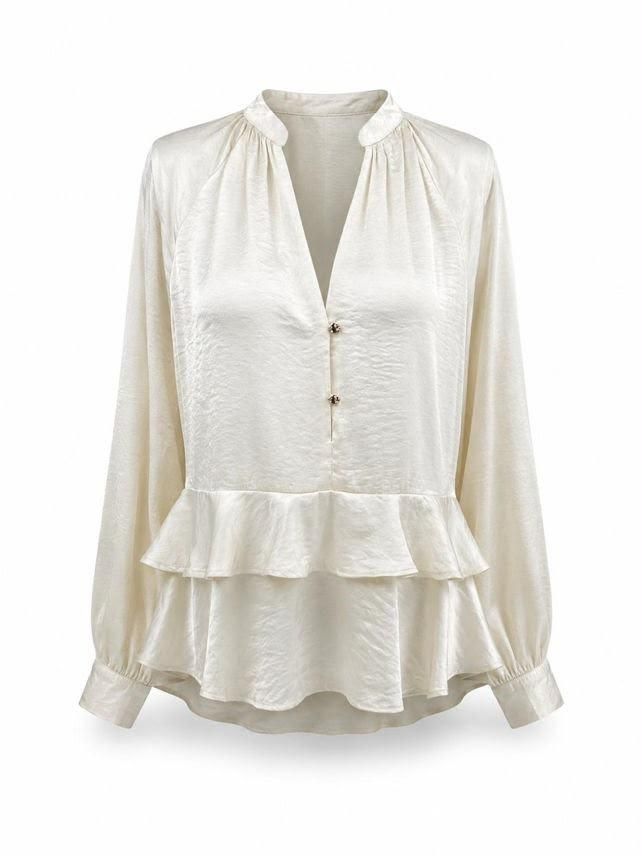 Blusa blanca de manga larga con pliegues en la parte delantera, bajo con volantes y detalle de botones.