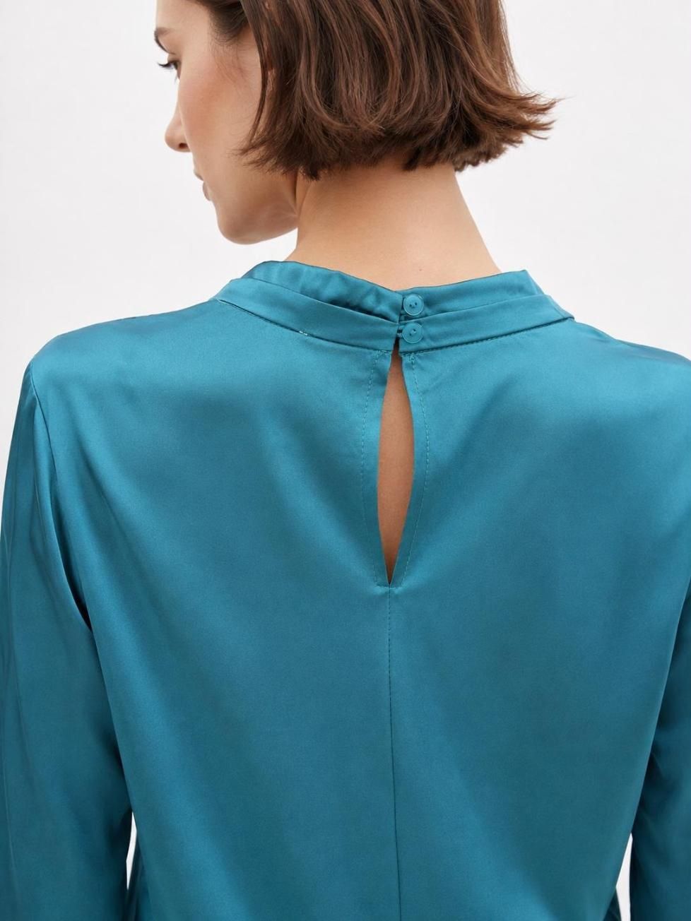 Mujer vista de espaldas con una blusa color turquesa con una pequeña abertura en forma de ojo de cerradura