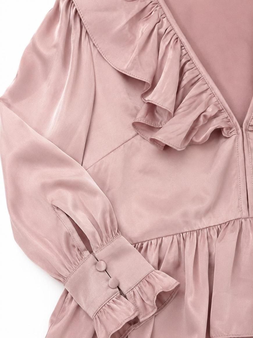 Primer plano de la manga de una blusa rosa con puños con volantes y detalle de botones en la muñeca.