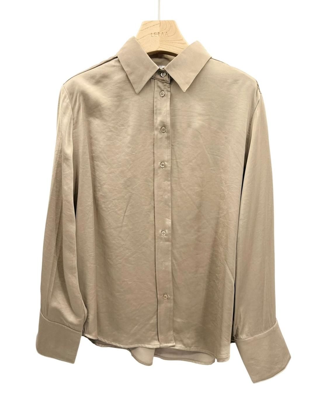 Camisa beige de manga larga con botones, colgada en una percha, vista frontal.