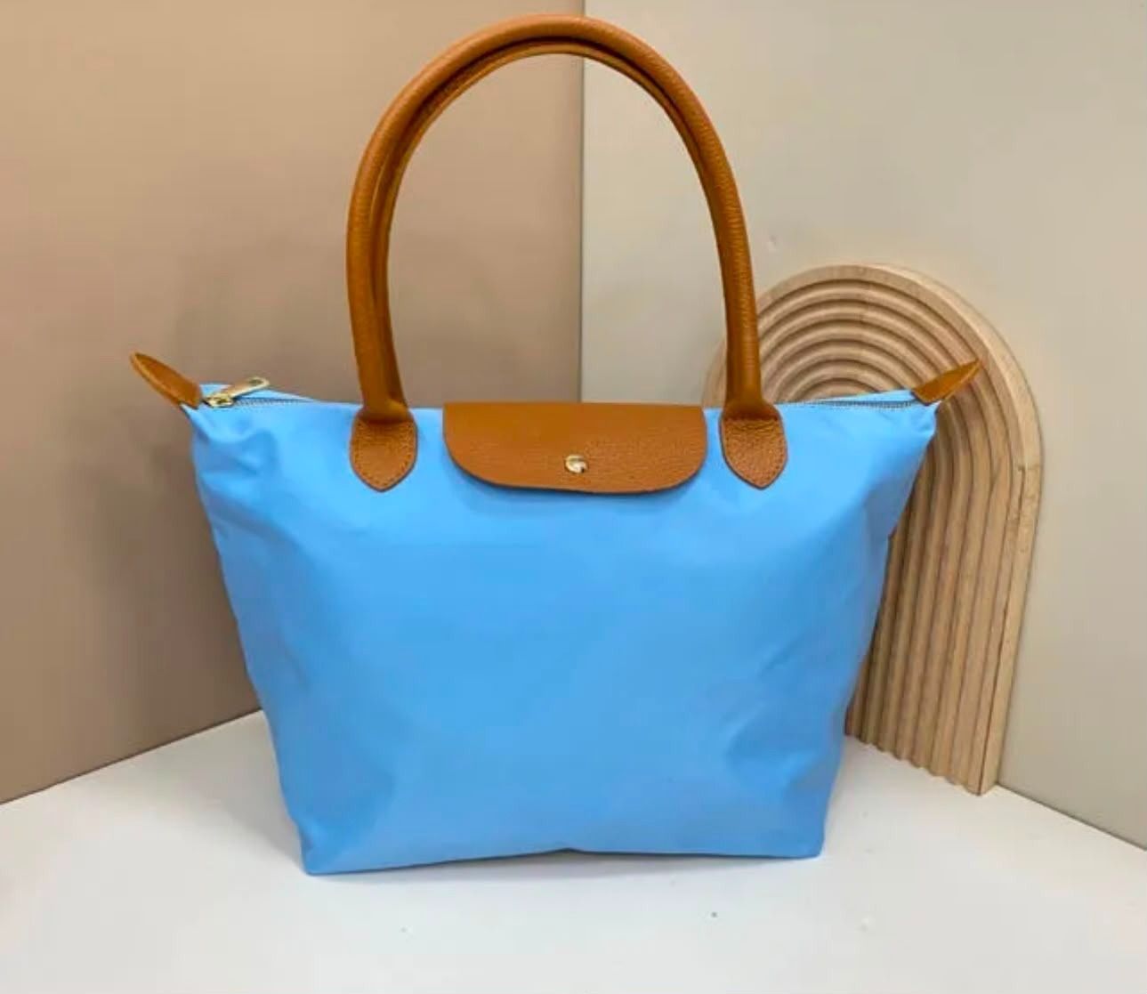 Bolso tote azul con asas y ribetes color tostado sobre una superficie blanca sobre un fondo beige.
