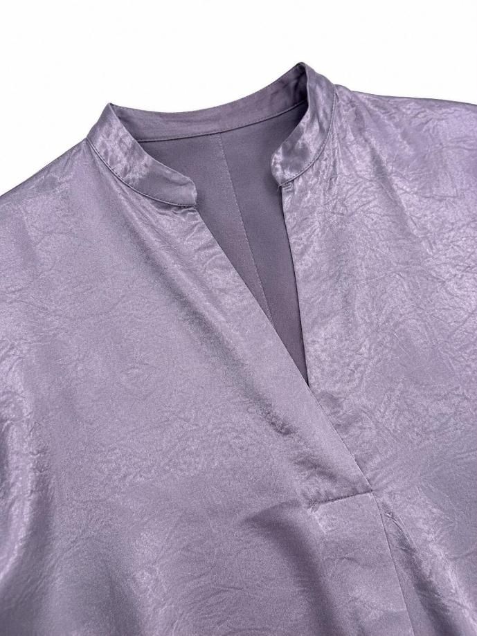 Primer plano de una blusa de satén color lavanda con escote en V y cuello dividido.