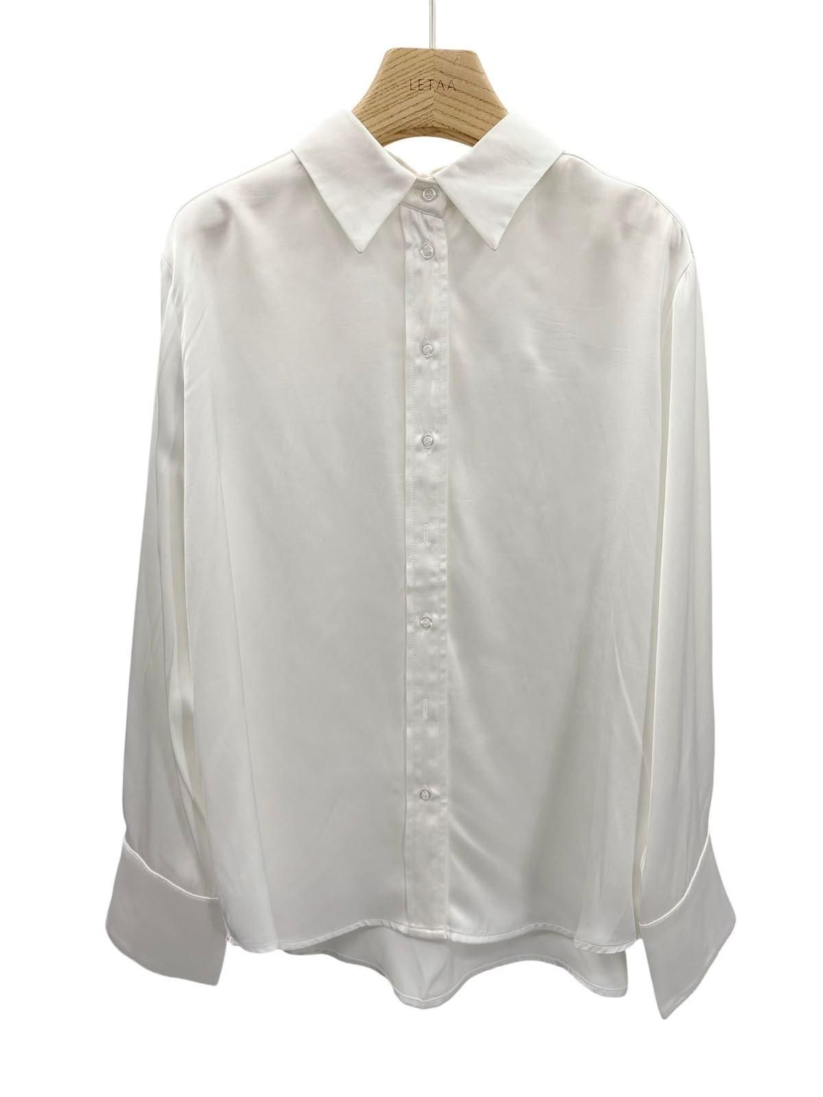 Camisa blanca de manga larga abotonada colgada en una percha de madera.