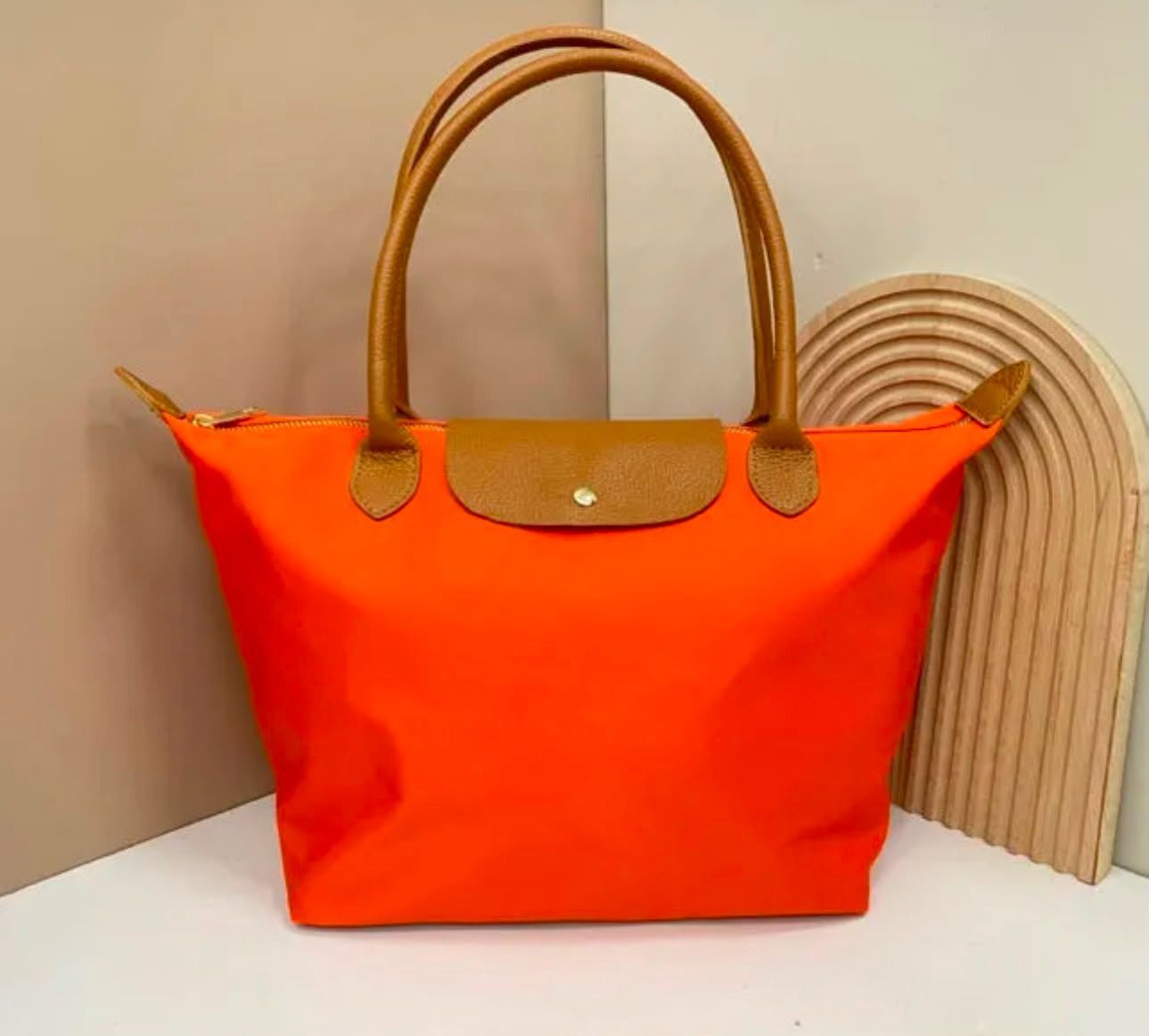 Bolso de mano de color naranja brillante con asas color canela sobre una superficie blanca