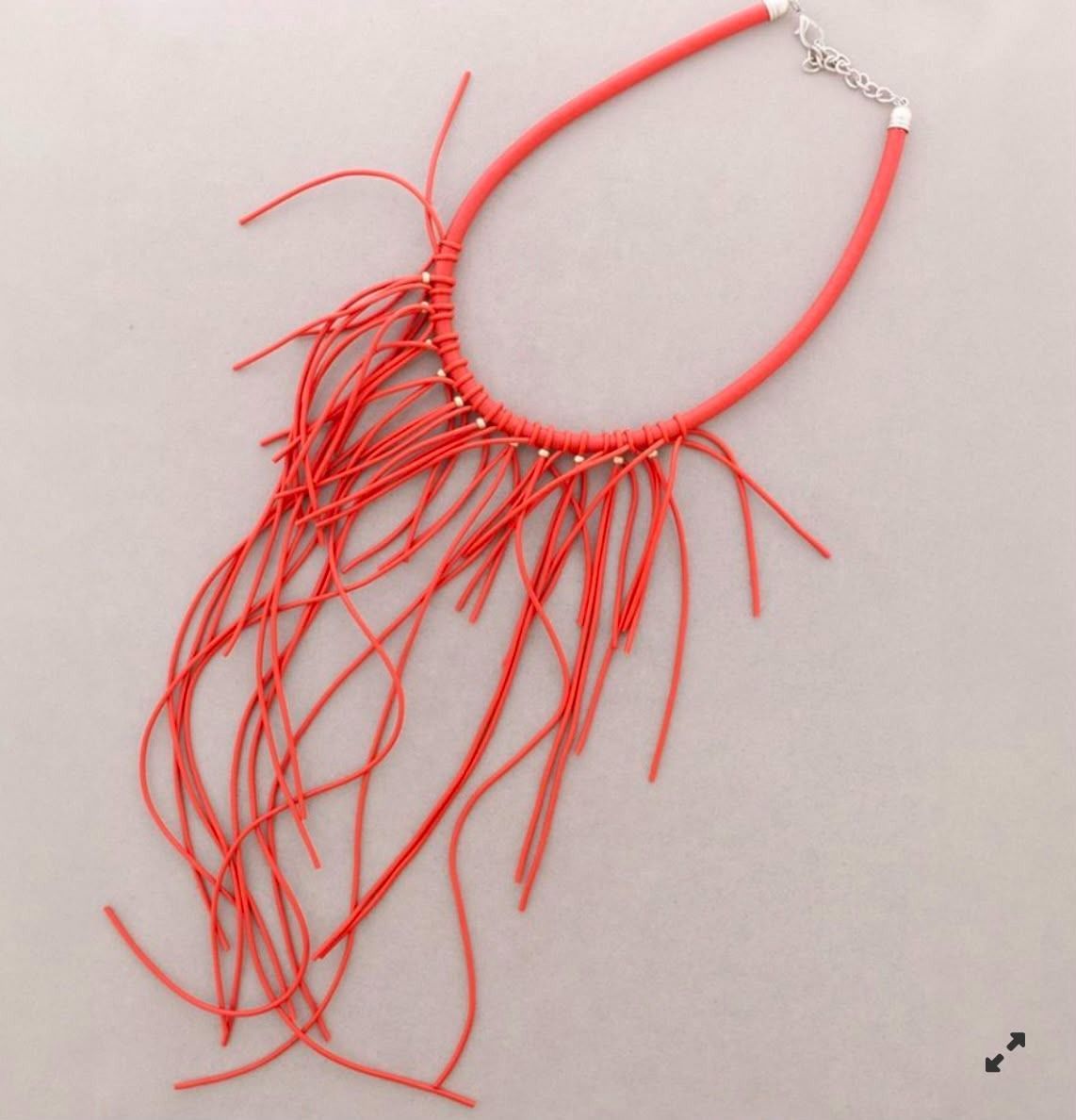 Collar rojo con largos cordones colgantes sobre un fondo claro.