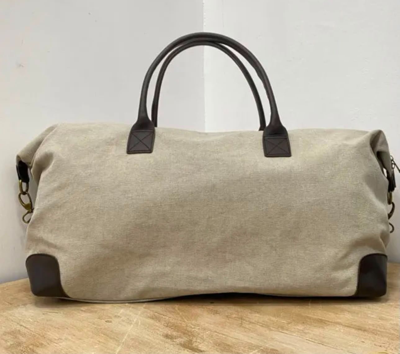 Bolsa de lona beige con asas marrón oscuro sobre una superficie de madera.