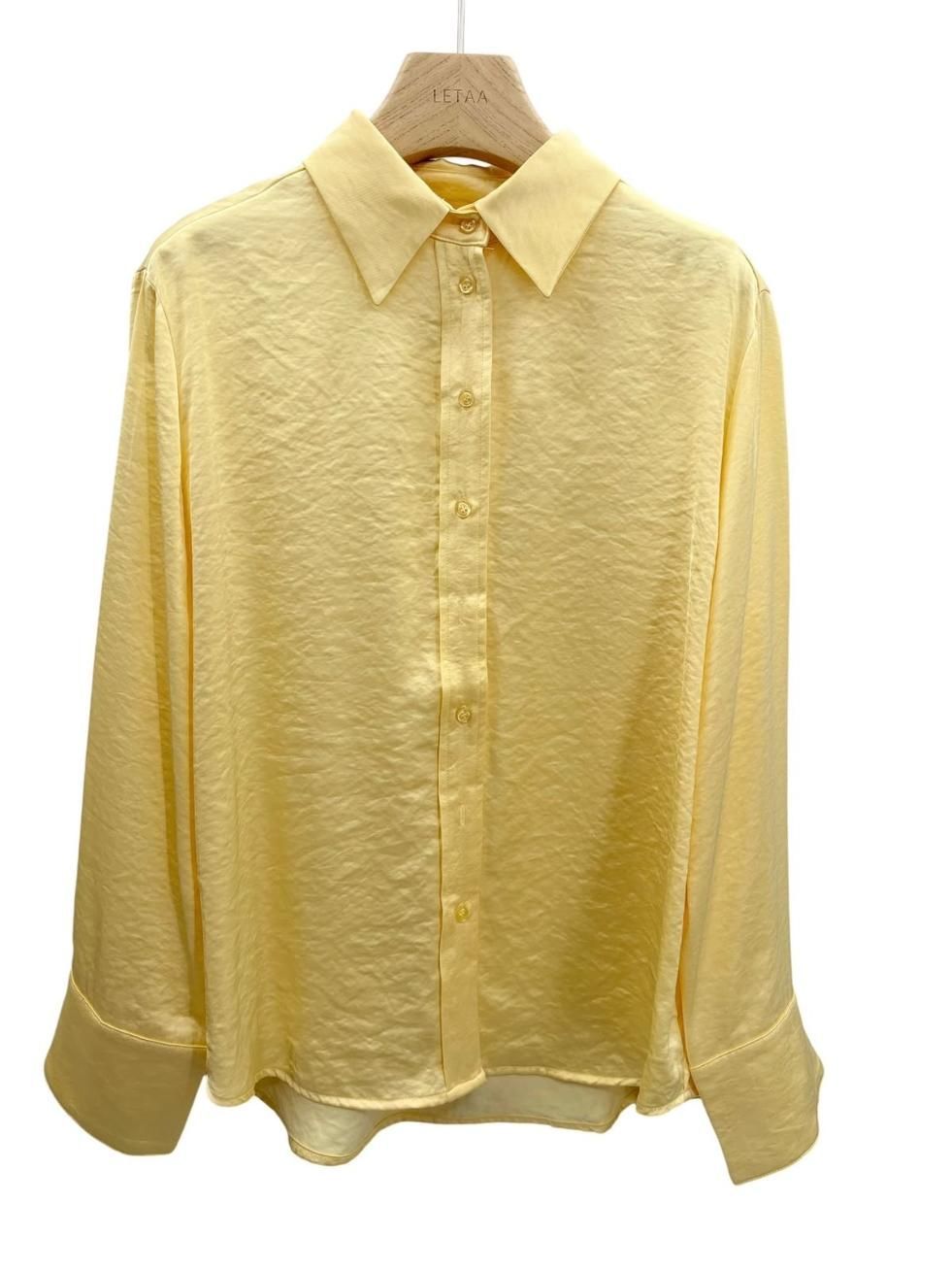 Camisa amarilla clara de manga larga con botones colgada en una percha.
