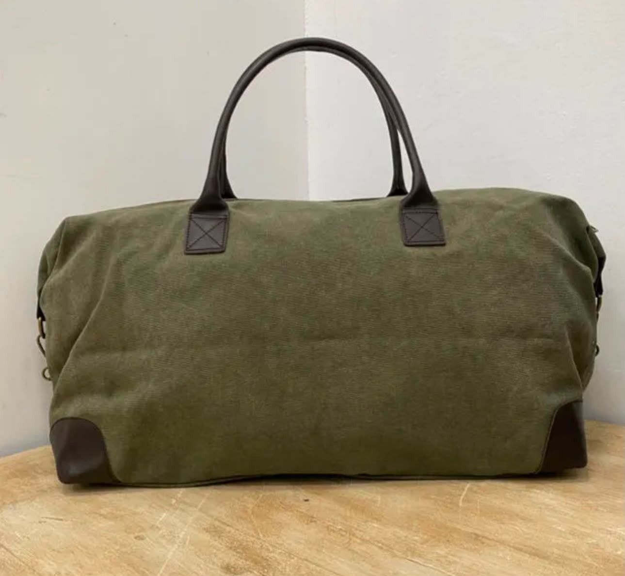Bolsa de lona verde oliva con asas negras sobre una superficie de madera.