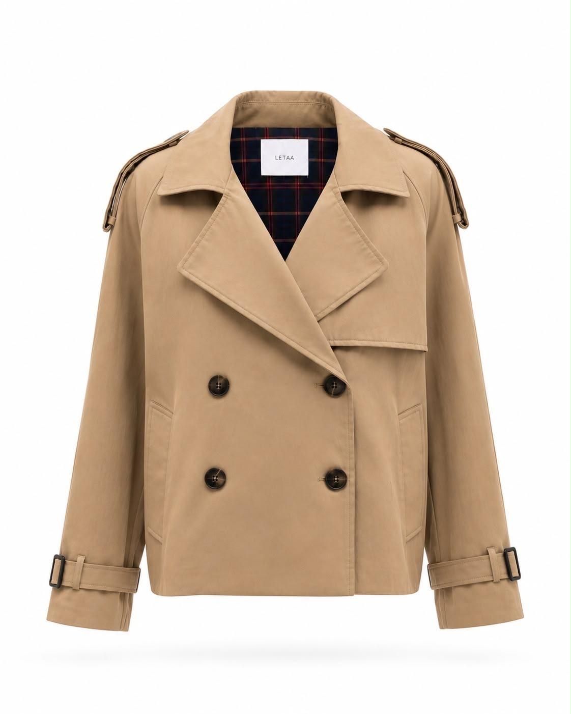 Gabardina beige de doble botonadura con solapas anchas, botones negros y tiras en los puños sobre fondo blanco.
