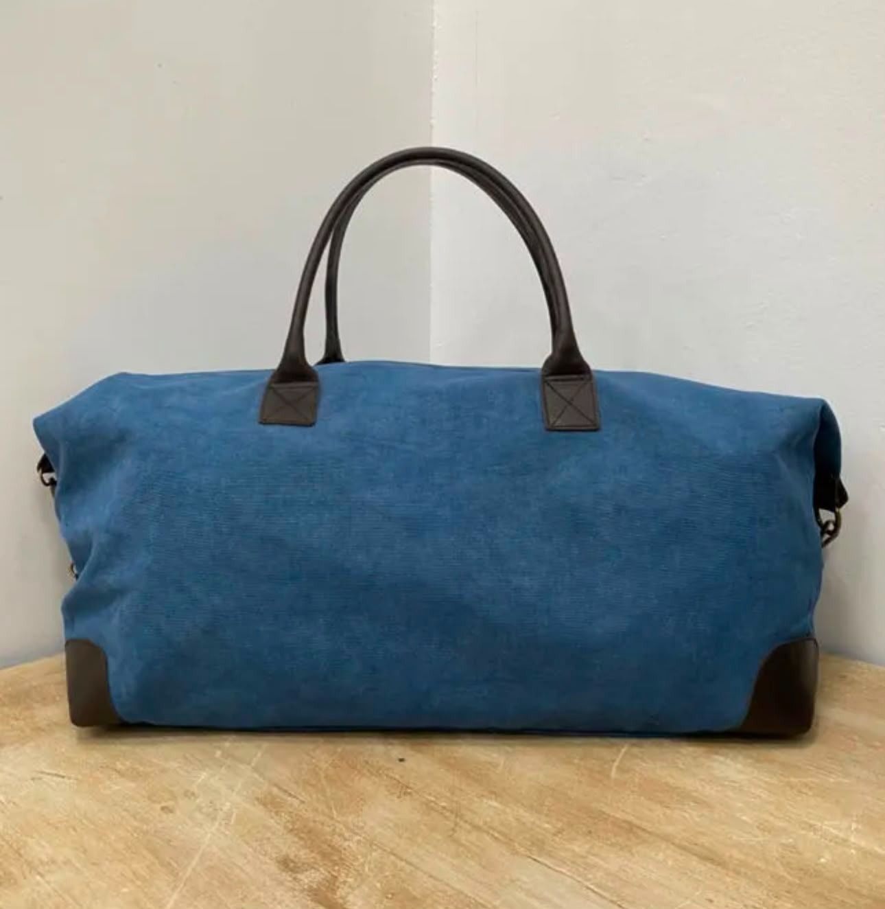 Bolsa de lona azul con asas marrones sobre un suelo de madera.