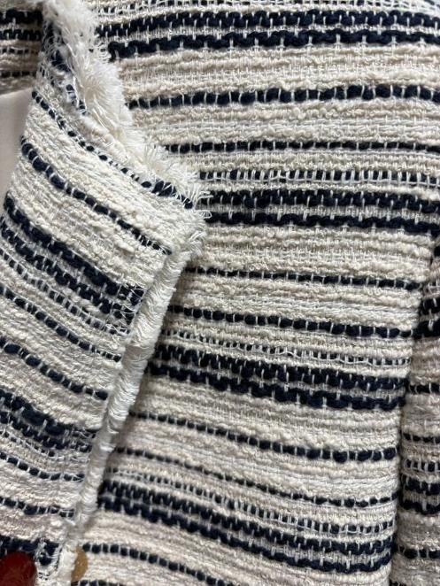 Primer plano de una chaqueta tejida a rayas negras, blancas y beige con solapa abotonada y tejido texturizado.