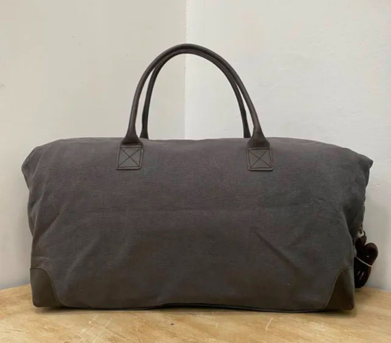Bolsa de lona gris con asas negras sobre un fondo claro liso.