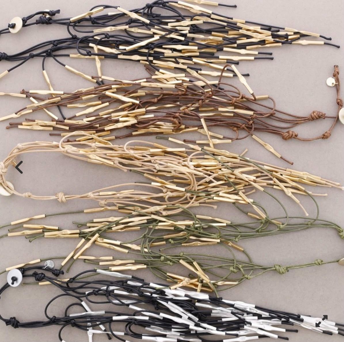 Cordones o collares variados, adornados con cuentas y trenzados, dispuestos en filas sobre una superficie clara.