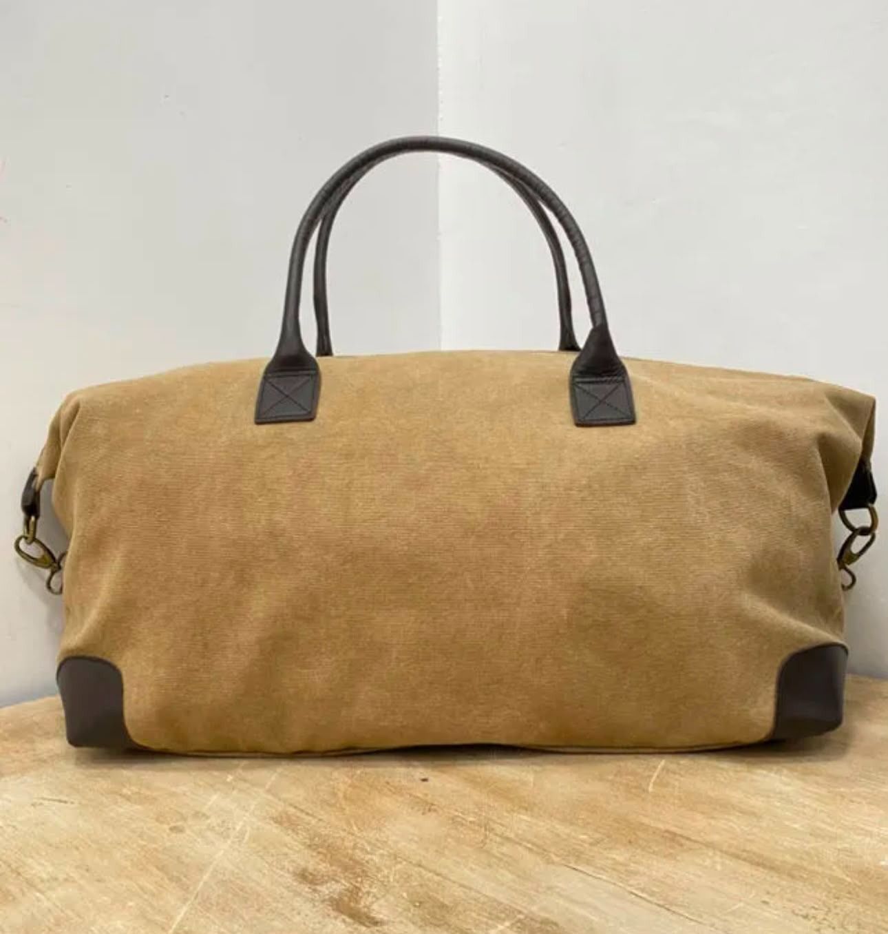 Bolsa de lona color canela con asas y ribetes de color marrón oscuro sobre una superficie de madera.
