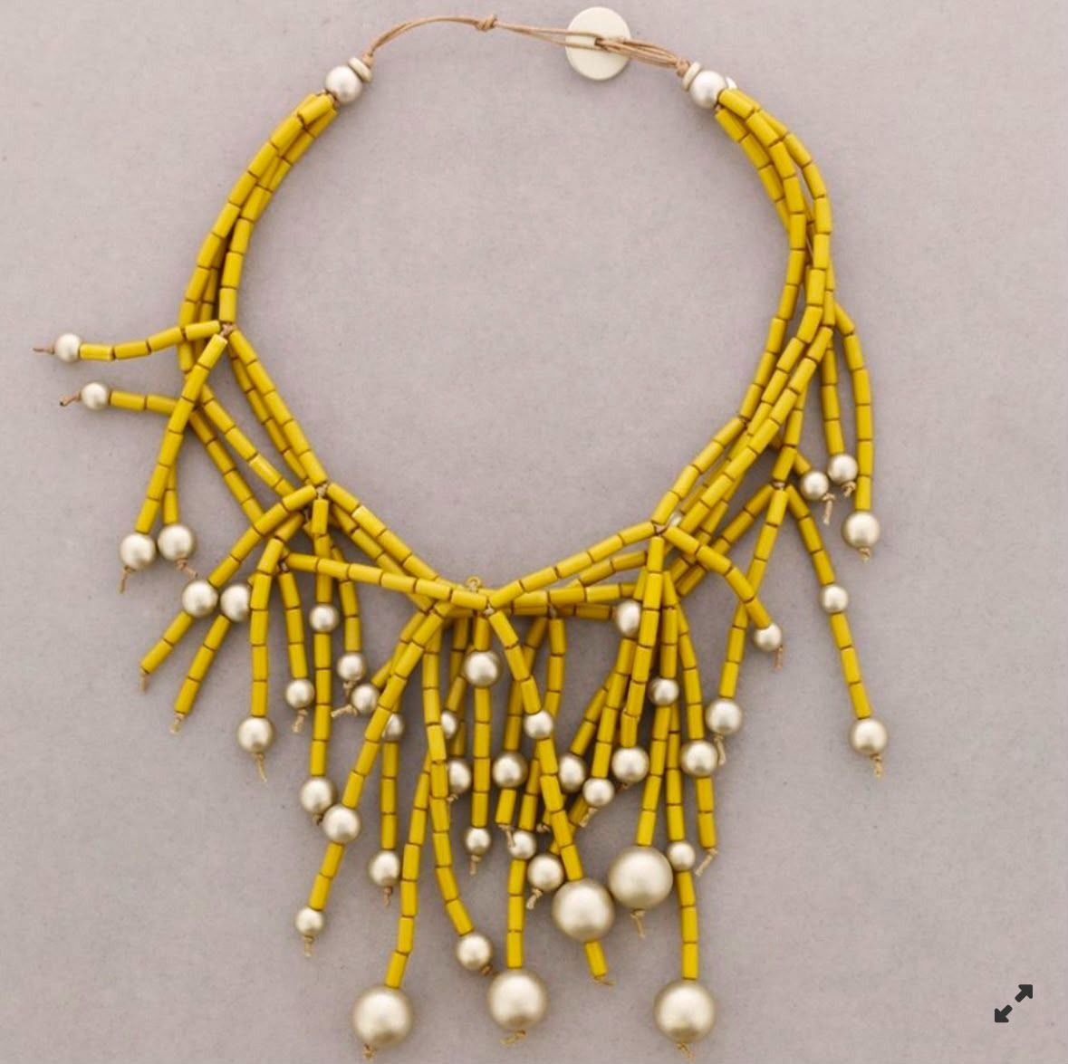 Collar de cuentas amarillas con colgantes blancos en forma de borla sobre un fondo beige.